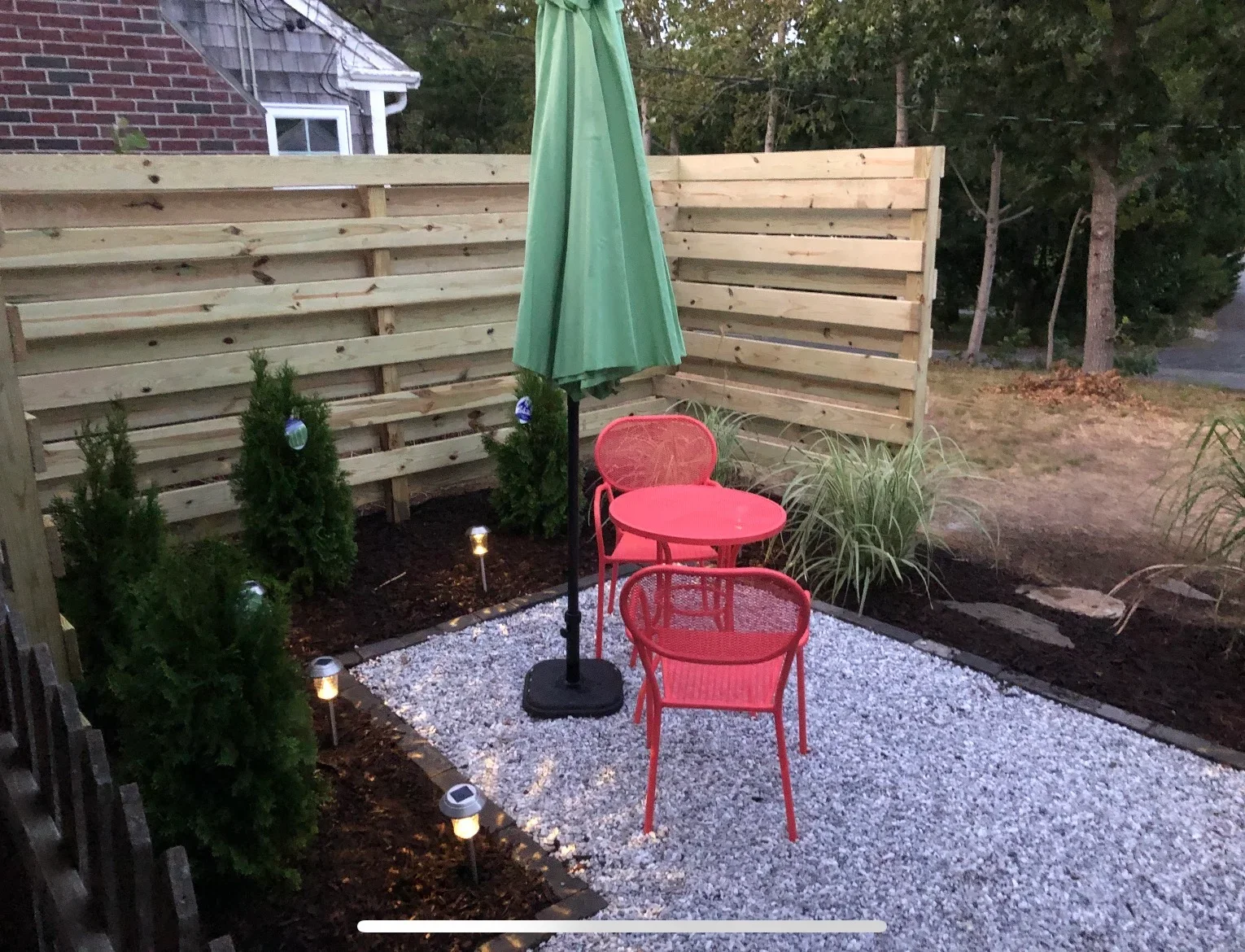 Horizontal wood fence with gravel patio, landscape lighting, and evergreen plantings