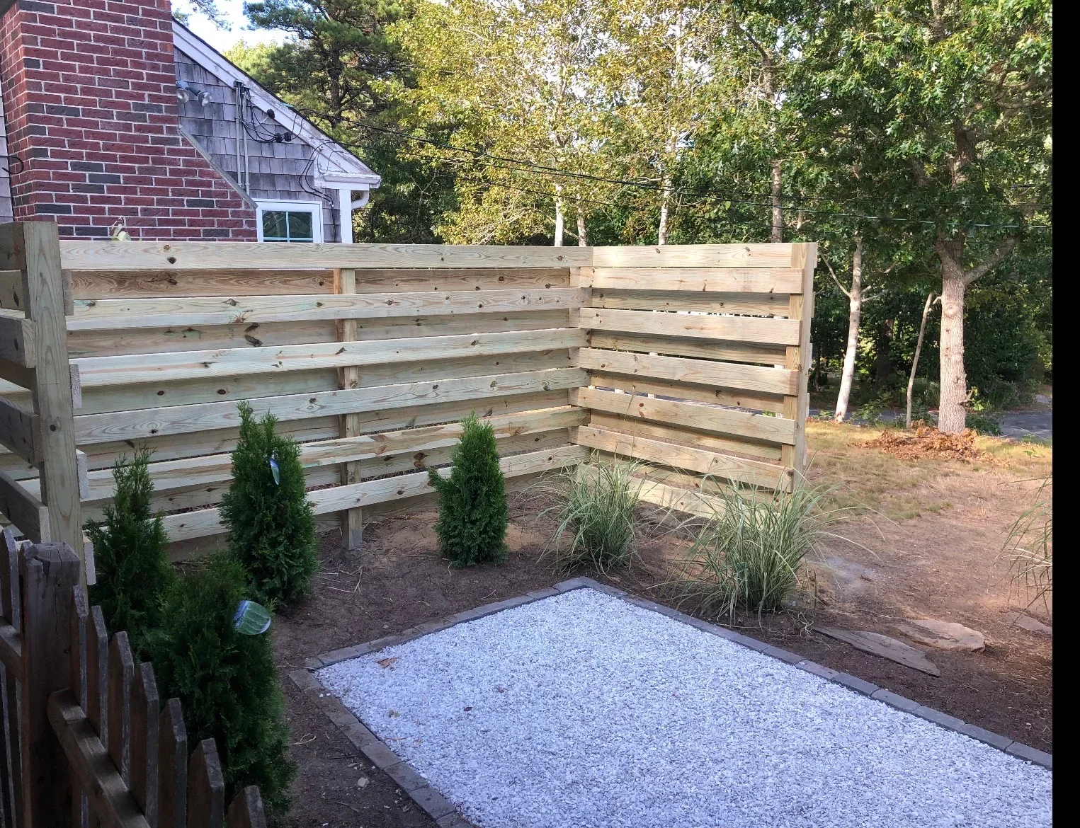 Horizontal wood privacy fence with gravel patio and landscape plantings