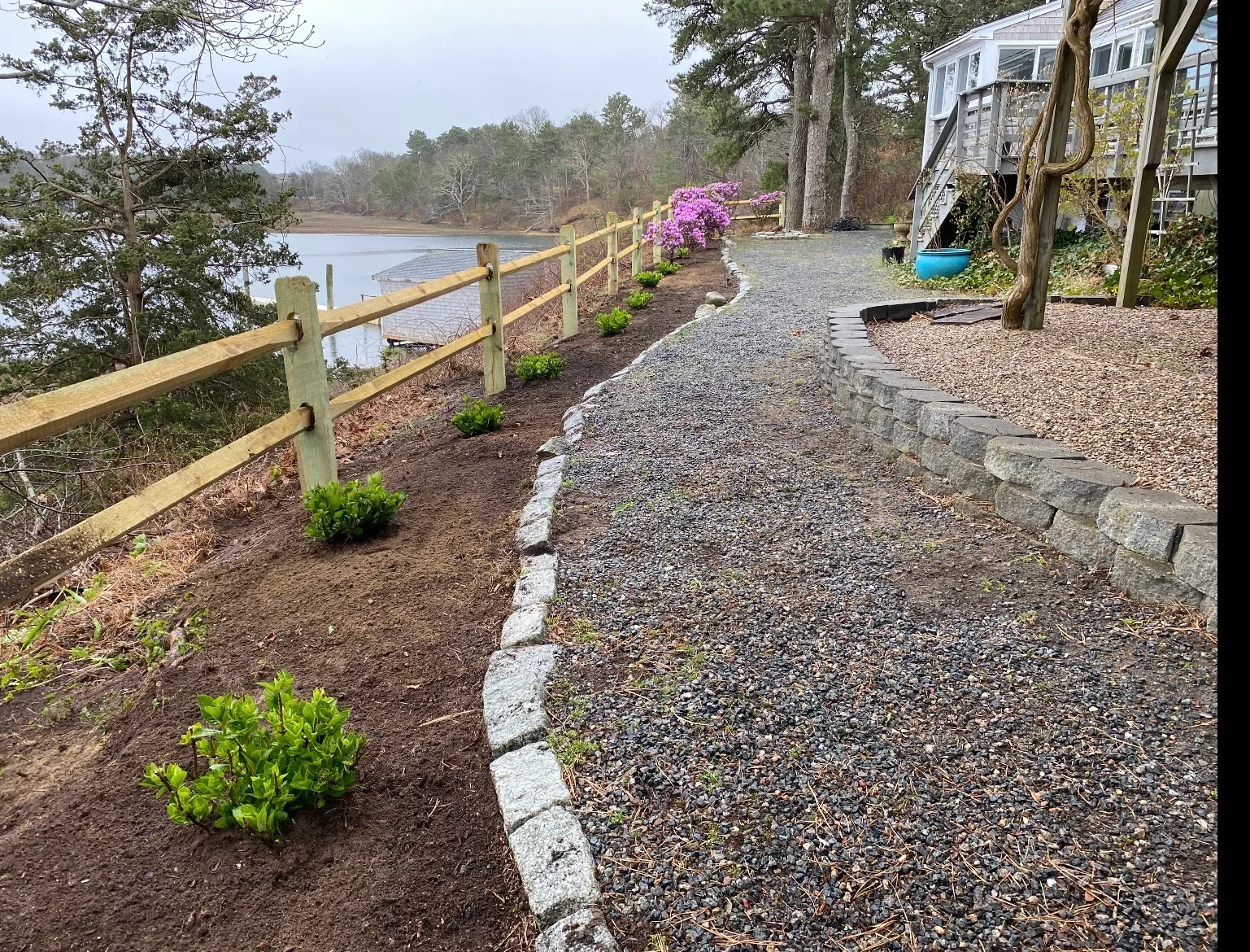 Gravel pathway with stone edging, wooden rail fence, and planted beds overlooking water