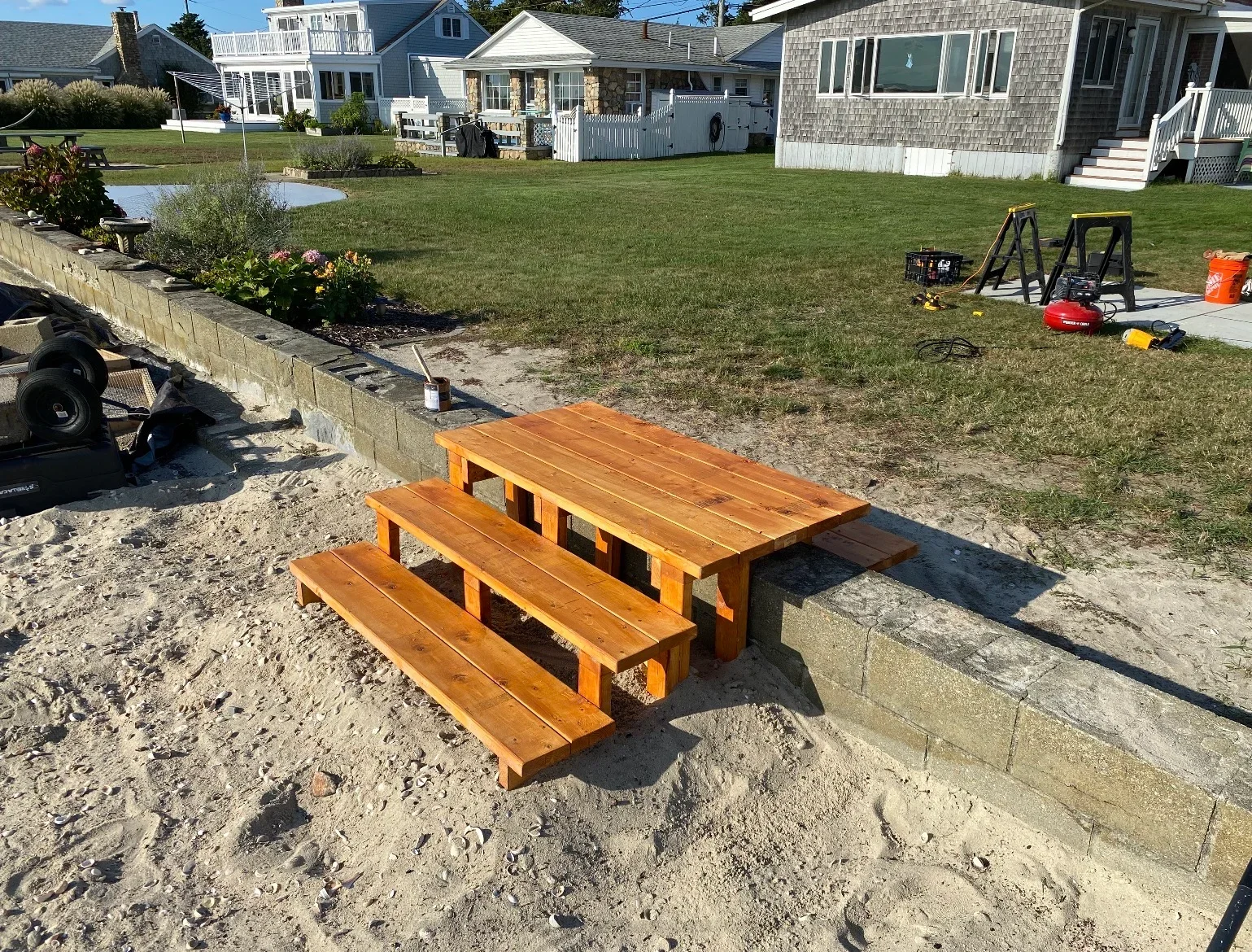 Custom wood picnic table with benches on sandy beach near concrete retaining wall